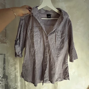 lila-randig skjorta - lila-randig skjorta med silvriga knappar och detaljer. ärmar går att kavla upp med spänne.