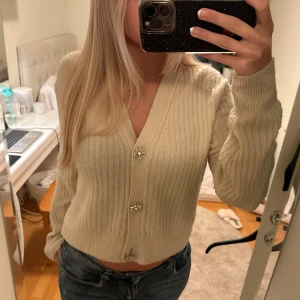 Beige ribbad kofta från H&M - Säljer en superfin beige ribbad kofta från H&M. Den har långa ärmar och snygga dekorativa knappar som ger en extra touch. Perfekt för höst och vinter när du vill hålla dig varm och stilren. Passar både till vardags och lite finare tillfällen. 🧥✨
