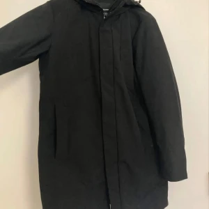 Svart jacka från Jack & Jones - Säljer en svart jacka från Jack & Jones. Den har en justerbar huva och stormmuddar för extra skydd mot väder och vind. Insidan är fodrad med återvunnet material och jackan har hybrid dun för extra värme. Perfekt för kalla dagar!