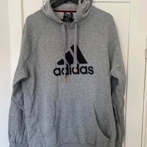 Grå hoodie från Adidas - Säljer en grå hoodie från Adidas i storlek L. Den är superbekväm och perfekt för både träning och chill. Hoodien har en klassisk Adidas-logga på framsidan och en justerbar huva med dragsko. Den är i bra skick och redo för nya äventyr!