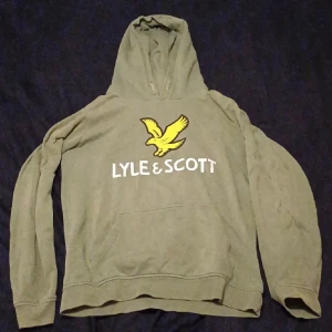 Grön hoodie från Lyle & Scott - Säljer en grön hoodie från Lyle & Scott i storlek 15/16 år. Den har en stor gul logga med en fågel på bröstet och texten 'LYLE & SCOTT'. Hoodien är långärmad och perfekt för en avslappnad stil. Den är i bra skick och redo för en ny ägare!