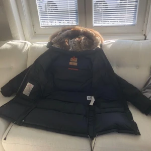 ÄKTA CANADA GOOSE!!! Ordinare pris 14999 kr,Svart pufferjacka med äkta  pälsdetaljer - Säljer en svart pufferjacka från Parajumpers. Den är perfekt för vintern med sin tjocka vaddering och pälsdetaljer runt huvan. Jackan har en dragkedja framtill och flera praktiska fickor. Den har också en snygg gul remdetalj vid kragen. Supervarm och stilren!