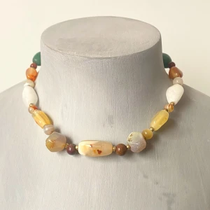 Färgglatt halsband med stenar - Säljer ett unikt och färgglatt halsband med stora, oregelbundna stenar i olika nyanser av gult, vitt, grönt och brunt. Perfekt för att ge en bohemisk touch till din outfit. Halsbandet har en härlig mix av färger och former som verkligen sticker ut!
