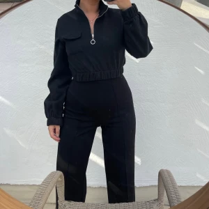 Svart croppad tröja med dragkedja - Säljer en stilren svart croppad tröja med en cool dragkedja framtill. Tröjan har långa ärmar och en elastisk midja som ger en snygg passform. Perfekt för både vardag och fest! Liten i storleken