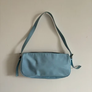 LJUSBLÅ VÄSKA - Ljusblå baguetteväska med glansig yta i bra skick från Nelly!! 