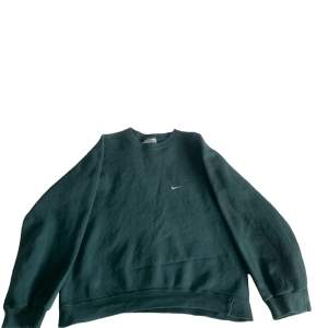 Säljer en grön sweatshirt från Nike i storlek S. Den har en klassisk design med långärmade ärmar och en liten Nike-logga på bröstet. Perfekt för en avslappnad stil eller träning. Materialet känns mjukt och bekvämt.