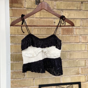 Svart och vit stickad topp från Zara - Säljer en superfin stickad topp från Zara i svart och vitt. Den har smala axelband och en söt volangdetalj framtill. Perfekt för en festlig kväll! Toppen är i nyskick och redo för nya äventyr.