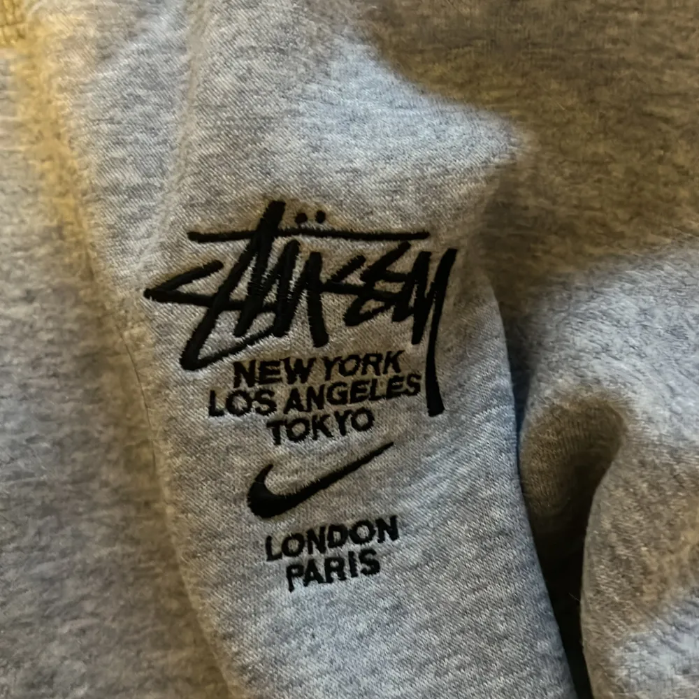 Säljer en grå sweatshirt från Nike i samarbete med Stüssy. Tröjan har en klassisk rund halsringning och är dekorerad med Stüssys ikoniska logga och städer som New York, Los Angeles, Tokyo, London och Paris. Vid snabb affär 550kr. Tröjor & Koftor.