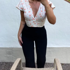 Vit blommig topp med volangärmar - Säljer en superfin vit topp med blommigt mönster i rosa och orange. Toppen har en v-ringad design och korta volangärmar som ger en söt och somrig look. Liten i storleken. Perfekt för både vardag och fest!