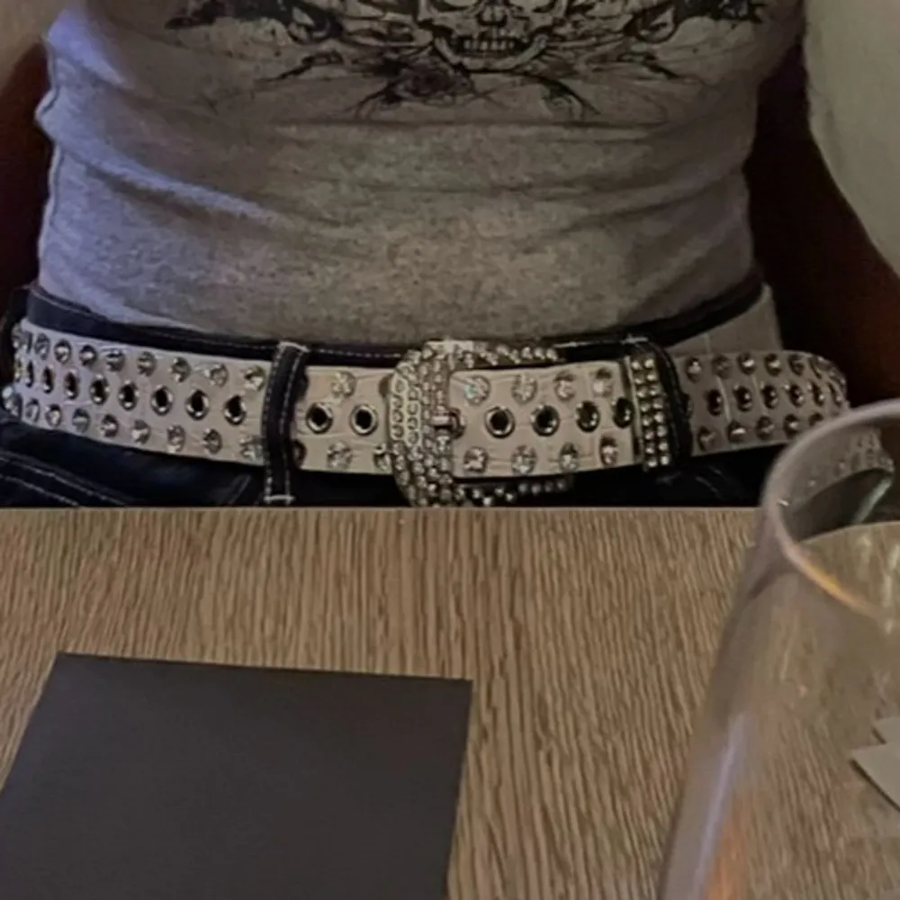 Säljer ett coolt vitt bälte med silverfärgade nitar och en glittrig spänne. Perfekt för att ge lite edge till din outfit! Passar bra till både jeans och kjol. Använd en hel del med ett fåtal skavanker men i bra skick.. Accessoarer.