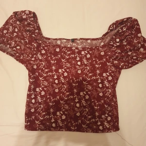 Röd topp - En röd blommig topp med puffärmar. Toppen är i en kort modell och har en avslappnad passform. Säljer för 50 kr