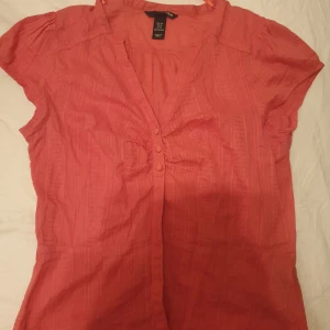 Rosa blus - En rosa blus med korta ärmar och knappar framtill. Blusen har en lätt detalj vid bröstet.Super fin oanvänd säljer för 70