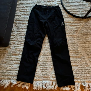 Svarta byxor från Haglöfs - Säljer ett par svarta byxor från Haglöfs. De är perfekta för utomhusaktiviteter med sin bekväma passform och elastiska midja. Byxorna har en enkel design och är gjorda i ett slitstarkt material.
