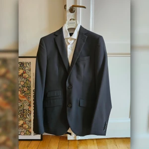 Riley Komplett Kostym Svart - Komplett kostym från Riley inklusive vit skjorta, storlek 46 (slim fit, skjorta super slim fit), skick 4/5. Fickor ej sprättade, kostympåse medföljer.