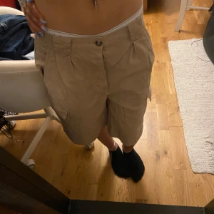 Beiga lång-shorts, knappar och bakfickor. Super söt och för både killar & tjejer. - Xs-s men väldigt liten i midjan, kanske xs eller Xxs. Dom e från tidigare 2000 talet men ganska så oanvända. Inga defekter.