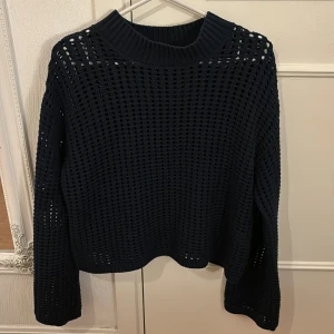 Marinblå stickad tröja från Holly & Whyte - Säljer en snygg marinblå tröja från Holly & Whyte. Den har ett coolt hålmönster och är perfekt för lager-på-lager-stil. Tröjan är långärmad och har en ribbad krage. Perfekt för höst och vinter!