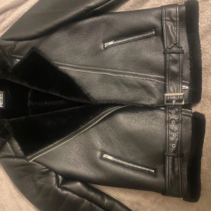 Svart skinnjacka från Pieces - Säljer en snygg svart skinnjacka från Pieces i mycket bra skick. Jackan har dragkedjor och ett bälte i midjan. Den är fodrad med mjuk päls för extra värme och har långa ärmar. Perfekt för höst och vinter!