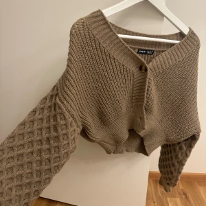 Brun stickad kofta - Säljer en superfin brun stickad kofta från Shein. Den har en unik design med olika stickmönster på ärmarna och kroppen. Koftan är perfekt för höst och vinter, och den har knappar framtill. Den är både mysig och stilren, perfekt för kalla dagar!