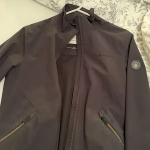 Svart Sailracing Jacka XS/S - Säljer en stilren svart vindjacka med dragkedja framtill. Jackan har långa ärmar och praktiska fickor med dragkedjor. Perfekt för höst och vår när det blåser lite extra. Passar både till vardags och lättare utomhusaktiviteter. 