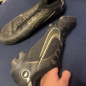 Svarta fotbollsskor Nike mercurical elite  - Säljer ett par svarta fotbollsskor med snygga gulddetaljer. Skorna har en tight passform och är perfekta för fotbollsträning eller match. De har snörning och är i bra skick, redo för nya äventyr på planen! Snöre finns till brevid . Prislappen kan diskuteras i pm 