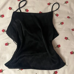 Svart topp - Snygg svart topp med tunna axelband. Perfekt för en utekväll eller fest. Materialet är mjukt och bekvämt, vilket gör den idealisk för sommarens varma dagar. Axelbanden knyts baktill (bild 2) och det finns även en dragkedja på sidan!
