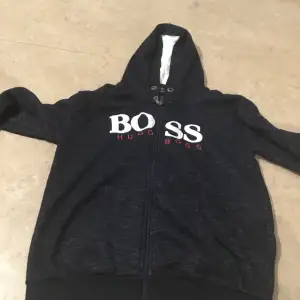 Säljer en snygg svart hoodie från Boss med vit och röd logga på bröstet. Den har en dragkedja framtill och en mysig huva med vitt foder. Perfekt för kyliga dagar eller som en stilren vardagströja. Passar både till jeans och joggers! Prisen kan diskutera.