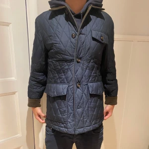 Mörkblå quiltad jacka - Säljer en snygg mörkblå quiltad jacka med knappar och en cool ficka på bröstet. Jackan har långa ärmar och en skön krage som skyddar mot kylan. Perfekt för höst och vår när det är lite kyligt ute. Passar både till vardags och lite finare tillfällen. Jackans märke är morris! Priset inte hugget i sten!