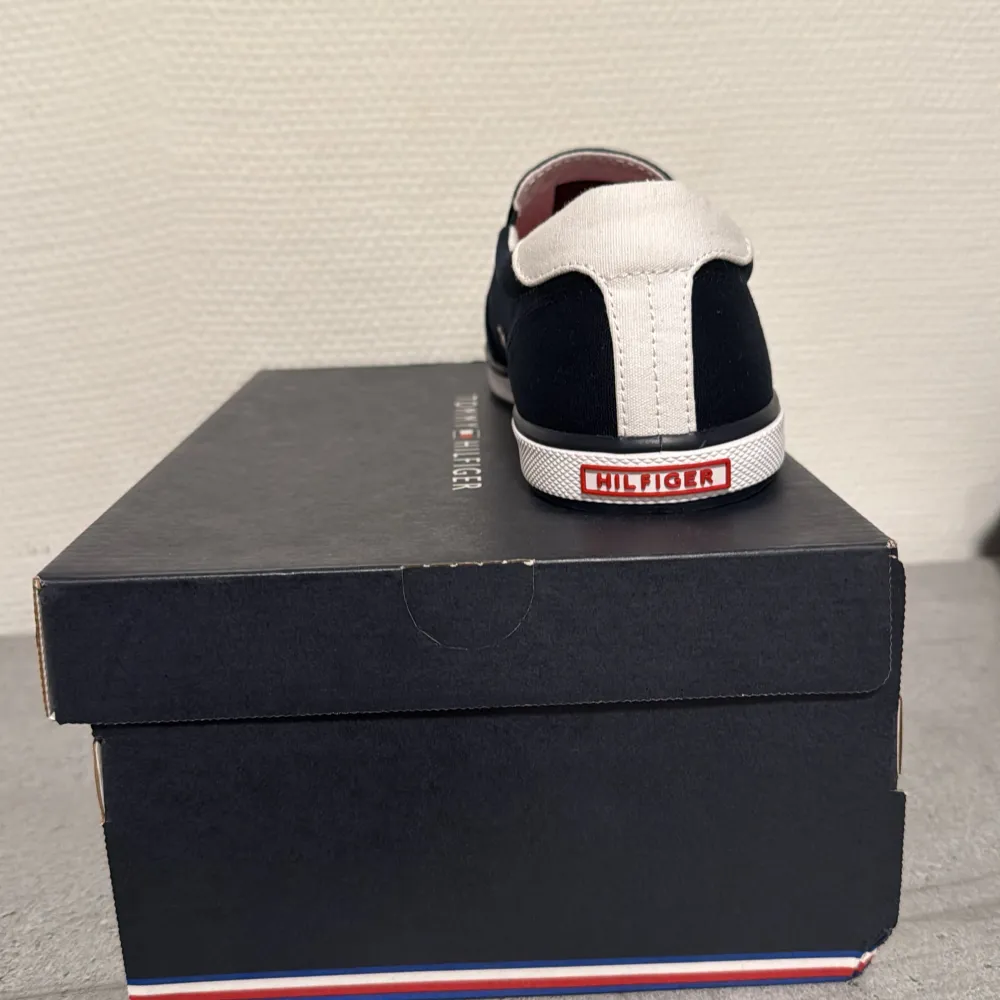 Snygga svarta sneakers från Tommy Hilfiger i helt nytt skick aldrig använt . De har en stilren design med vita detaljer och en röd sula. Perfekta för både vardag och fest. Skorna har en bekväm passform och är lätta att matcha med olika outfits.. Skor.