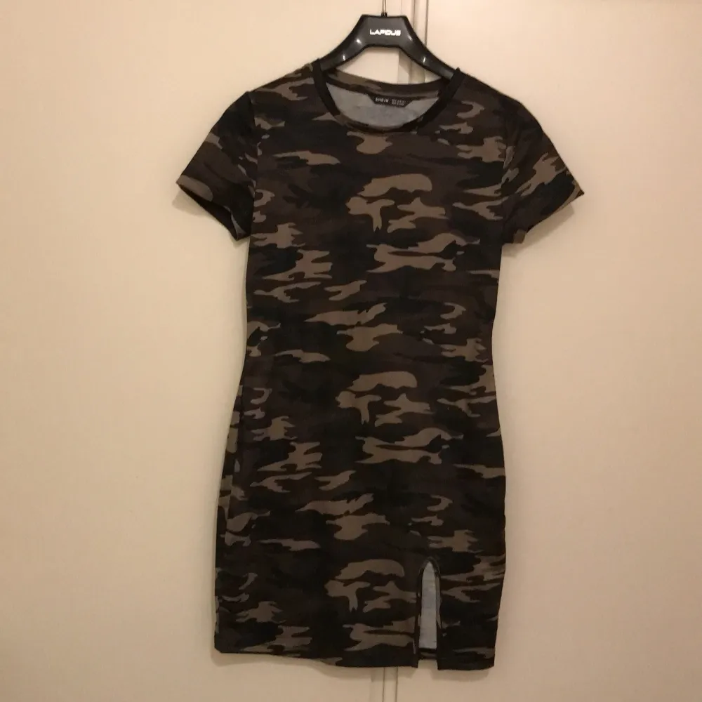 Snygg och trendig kortärmad klänning i camouflage. Den har en liten slits framtill och är perfekt för en avslappnad stil. Materialet känns mjukt och bekvämt, perfekt för vardagsbruk eller en cool utekväll.. Klänningar.