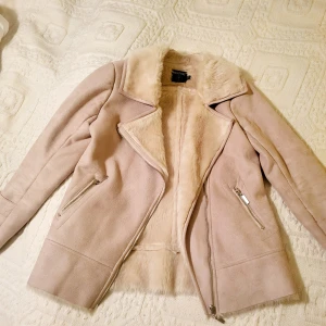 Beige sherlingjacka - Säljer en superfin beige jacka från med mjuk fuskpäls på insidan. Den har en snygg dragkedja och två fickor med dragkedjor. Fodret i fickorna har tyvärr hål i sig, annars inga tecken på användning. Perfekt för höst och vinter.