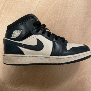 Nike Air Jordans i svart, mörkblått och vit - Säljer ett par Nike Air Jordans i svart och vit. Skorna har en klassisk design med snörning och är i bra skick. Perfekta för både vardag och fest! Storlek dam 38. 