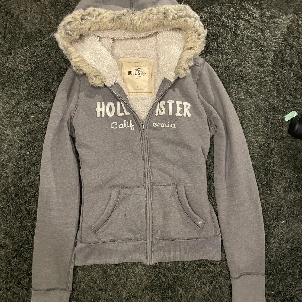 Hoodien har haft hål i fickan som jag har lagat med en ladderstich. Kontakta för flera närbilder på de ihopsydda hålen. Grå zip up hoodie från Hollister med päls/ fur. Jag vet inte riktigt vad den är värd så priset är nog ganska förhandlingsbart. Om ni skriver till mig privat så kan jag också skicka bild påbhur den passar på mig. Den passar bra på mig och jag är xxs, tror den skulle funka för xxxs-s. Kan också mötas upp i istället för att skicka, bor i stockholm.. Hoodies.