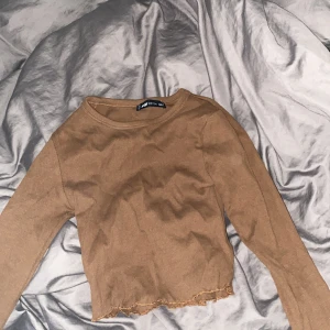 Brun ribbad tröja från FB Sister - Säljer en snygg brun ribbad tröja från FB Sister i storlek XS. Den har långa ärmar och en croppad design med råa kanter. Perfekt för höst och vår, och funkar både till vardags och fest. Superbekväm och lätt att matcha med jeans eller kjol!