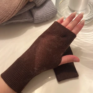 Bruna stickade torgvantar - Säljer ett par mysiga bruna halvvantar i stickat material. Perfekta för att hålla händerna varma medan fingrarna är fria. De har en ribbstickad mudd som sitter skönt runt handleden. Passar perfekt för kyliga dagar när du vill ha lite extra värme utan att tappa fingerfärdigheten.