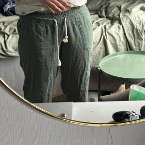 Gröna linnebyxor med snörning från Roxy - Säljer ett par gröna linnebyxor från Roxy i bra skick. De har en bekväm loose passform och är perfekta för sommar och vår. Byxorna har en elastisk midja med snörning för justerbar passform. De är både stiliga och avslappnade, perfekta för en chill dag ute eller hemma.