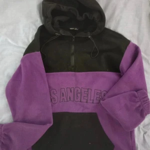 Svart och lila hoodie med Los Angeles-tryck - Säljer en snygg och bekväm hoodie från Boohoo i svart och lila. Den har ett coolt Los Angeles-tryck över bröstet och en praktisk dragkedja framtill. Perfekt för en avslappnad stil eller en dag på stan. 🖤💜