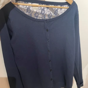Mörkblå kofta med spetsdetaljer - Säljer en elegant mörkblå kofta med spetsdetaljer på baksidan. Den har långa ärmar och knappar framtill. Perfekt för både vardag och festliga tillfällen. Superfin att matcha med jeans eller kjol! 💙