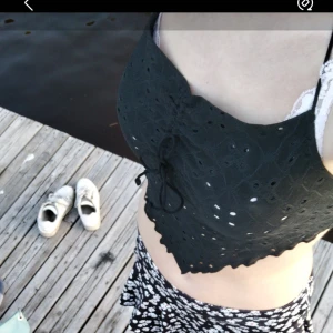 Svart broderad croppad topp - Snygg svart croppad topp med broderade detaljer och knytning. Perfekt för sommardagar vid vattnet eller en avslappnad dag i solen. Toppen har en unik design med små hål och en söt rosett fram.