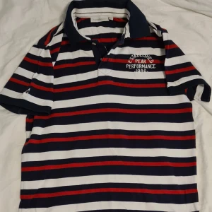 Sommar25. Randig pikétröja från Peak Performance M - Säljer en snygg randig pikétröja från Peak Performance i storlek M. Tröjan har ett klassiskt mönster i marinblått, vitt och rött med en broderad logga på bröstet. Perfekt för en avslappnad stil eller en dag på golfbanan. Kvaliteten är riktigt bra och den är i mycket bra skick!