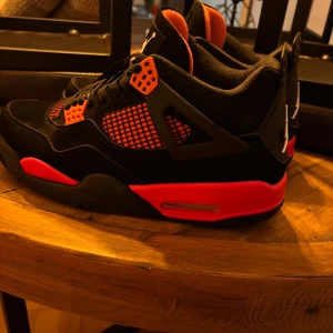 Jordan 4 Red Thunder - Säljer ett par snygga Jordan 4 red thunder som är en blandning mellan svart och rött.  Väldigt bra skor nu inför vintern.  Skorna är i storlek 45 men sitter som 44.Skorna har en cool design med snörning och den klassiska Jumpman-loggan på baksidan. Perfekta för både vardag och fest! De är i mycket bra skick och redo för nya äventyr. Ps box osv kommer tyvärr inte med därav priset. Tar även byten