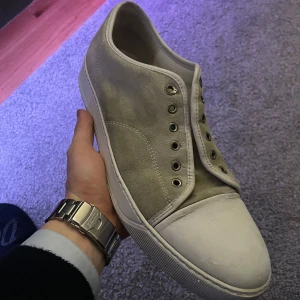 Grå sneakers från Lanvin - Säljer ett par stilrena grå sneakers från Lanvin i mocka. De har en klassisk design med vita sulor. Perfekta för både vardag och festliga tillfällen. Skorna är i bra skick med lite slitage på sulorna.
