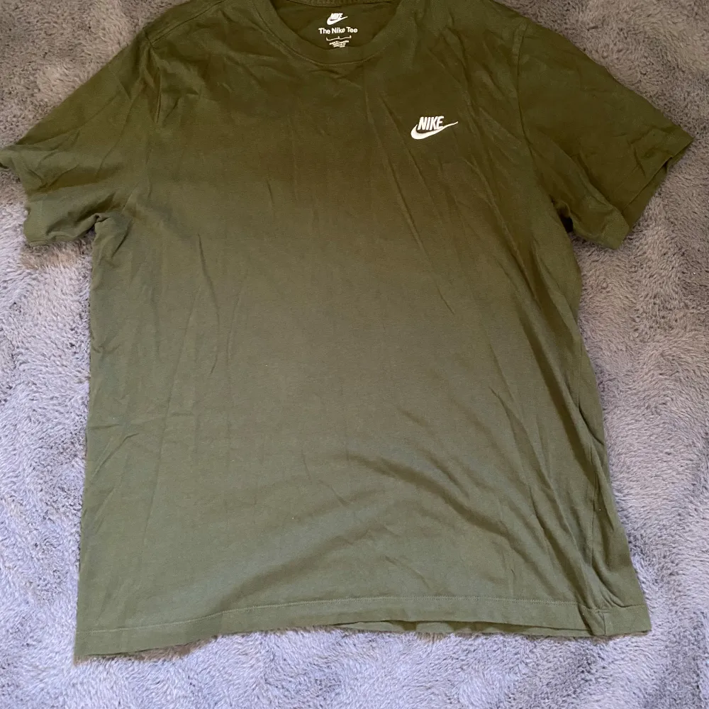 Säljer en olivgrön t-shirt från Nike i bra skick. Den har en klassisk passform med korta ärmar och en liten vit Nike-logga på bröstet. Perfekt för vardagsbruk eller träning. Skön och enkel stil som funkar året runt!. T-shirts.