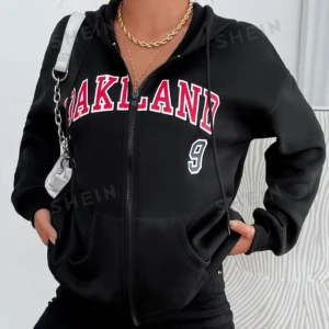 Svart hoodie med tryck från Shein - Säljer en svart hoodie från Shein med texten 'OAKLAND' i rött och vitt på framsidan. Den har en dragkedja och en luva, perfekt för en casual look. Stor och bekväm med fickor framtill. Passar perfekt till höst och vår!