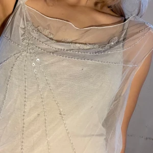 Vit topp med transparenta detaljer - Säljer en elegant vit topp med söta detaljer och broderier. Toppen har en unik design med ett lager av tunt tyg över axlarna och bröstet. Perfekt att ha utanpå ett linne, för sommarens fester eller en stilfull vardagslook. Passar bra till jeans eller kjol. 
