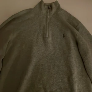 Grå tröja från Polo Ralph Lauren - Säljer en stilren grå tröja från Polo Ralph Lauren i storlek M. Tröjan har en halv dragkedja och är perfekt för både höst och vinter. Den är i mycket bra skick och är använd ett fåtal gånger. Tröjan har en klassisk design med det ikoniska logotypbroderiet på bröstet.