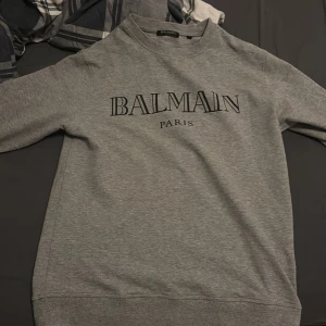 Grå sweatshirt från Balmain - Säljer en stilren grå sweatshirt från Balmain. Tröjan ser helt ny ut men den ända problemet är att den har krympts i tvätten. Modellen är M men nu skulle jag säga att den ligger mellan s/xs. Nypris 5000kr (pris kan diskuteras)