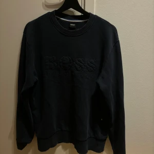 Svart tröja från Hugo Boss - Säljer en stilren svart tröja från Hugo Boss i storlek M. Tröjan har en diskret broderad logga på framsidan och är gjord i ett mjukt material. Perfekt för både vardag och fest. Passar bra till höst och vinter.