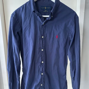 Blå skjorta från Ralph Lauren - Snygg blå skjorta från Ralph Lauren i slim fit. Skjortan har långa ärmar och knappar framtill. Perfekt för en stilren look.