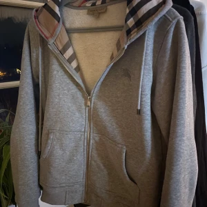 Burberry hoodie grå - Säljer en stilren grå huvtröja från Burberry med dragkedja och klassiskt rutigt mönster i huvan.    Kom prov för priser och frågor 💯💯💯