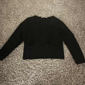 Svart glittrig topp - Snygg svart glittrig topp med v-ringning och långa ärmar. Perfekt för en kväll ute eller en festlig tillställning. 